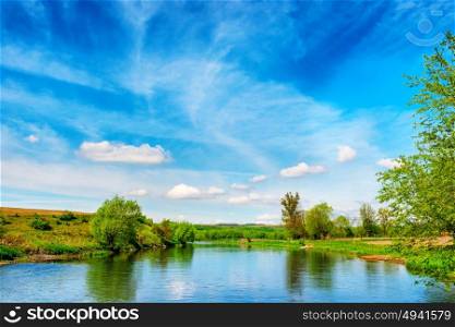 View to river banks with green trees and blue cloudy sky