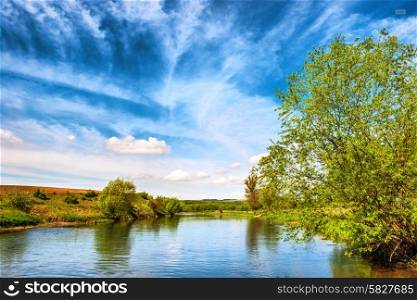 View to river banks with green trees and blue cloudy sky