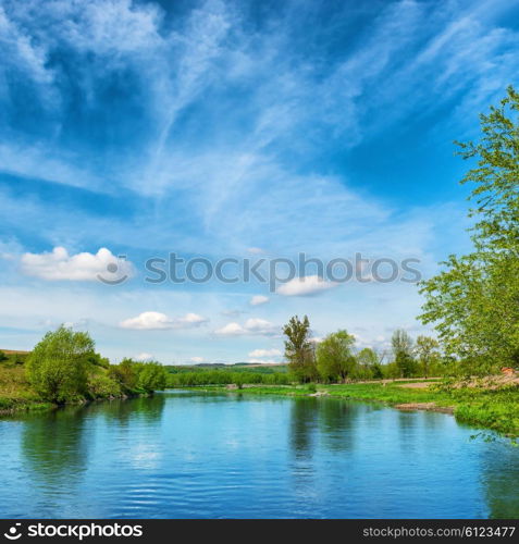 View to river banks with green trees and blue cloudy sky