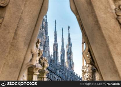 View to spires and statues on roof of Duomo through ornate marble fencing. Milan, Italy
