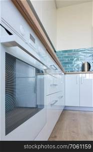 View to the bottom of the white kitchen with oven and brown floor. New and modern kitchen in bright colors