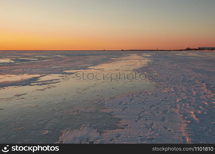 View to the frozen beach of Baltic sea and pier of Parnu on horizon in the light of sunset on sunny and cold winter evening, Estonia