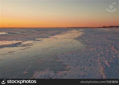 View to the frozen beach of Baltic sea and pier of Parnu on horizon in the light of sunset on sunny and cold winter evening, Estonia