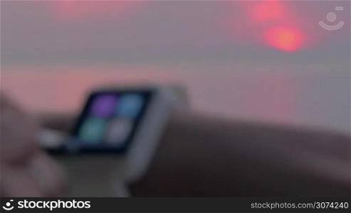 View to the sunset over sea with following close-up shot of woman using smartwatch and setting home city
