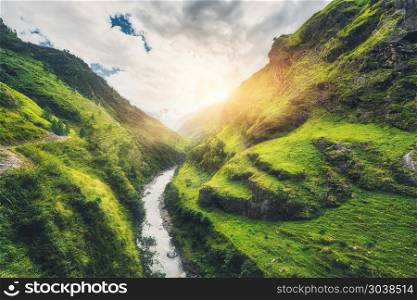 View with amazing mountains covered green grass, river, meadows and forest, blue sky with clouds, sun in autumn in Nepal at sunset. Mountain valley at bright sunny evening. Travel in Himalayas. Nature. Amazing mountains covered green grass, river at sunset