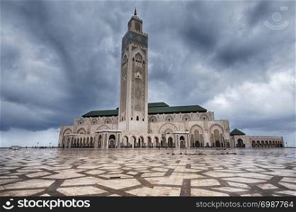 Viewed over a huge plaza made of granite stone on a dark and cloudy day, the Hassan II Mosque in Casablanca, Morocco is one of the largest mosques in the world.