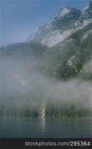 views of forest among fog in border of the lake with a waterfall