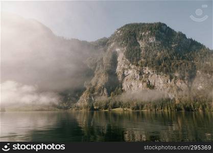 views of forest in the mountain among fog in border of the lake