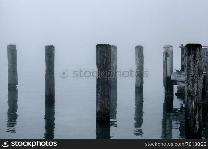 Views of the wooden pier in the mist on the Konigsee lake of Germany with wooden posts that get lost in the fog