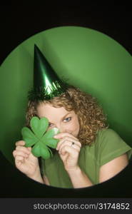 Vignette of young adult Caucasian woman on green background wearing Saint Patricks Day hat and holding shamrock.