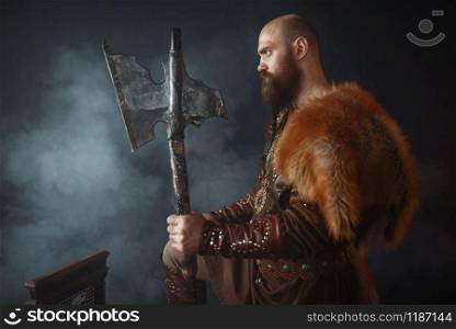 Viking with axe, martial spirit, barbarian image, side view. Ancient warrior in smoke on dark background