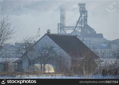 village house in winter on the background of an industrial factory.