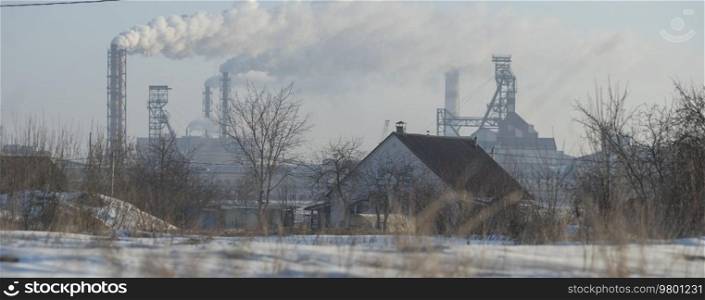 village house in winter on the background of an industrial factory.