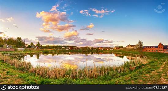 Village lake tranquil panorama. Sunset reflection in calm water. Historic buildings in Priluki town, Belarus