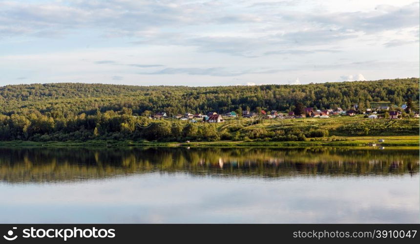 Village on river bank, reflections in water and solar day, siberia, russia