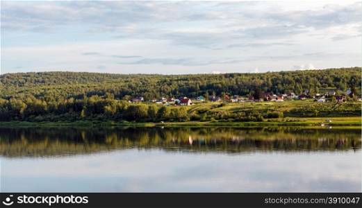 Village on river bank, reflections in water and solar day, siberia, russia