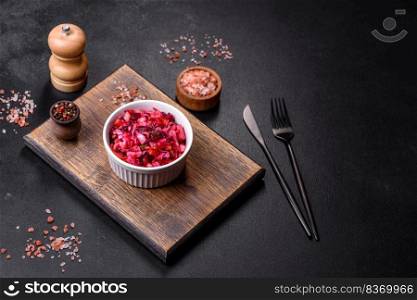Vinaigrette,  raditional ukrainian beetroot salad with boiled vegetables, pickled cucumbers, sour cabbage, olive oil and green canned peas. Vegetarian healthy dinner. Traditional ukrainian beetroot salad vinaigrette on a white plate on a black concrete or slate background