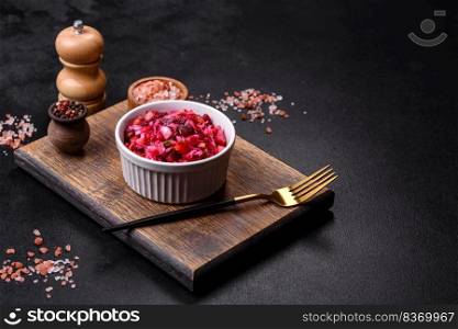 Vinaigrette, ?raditional ukrainian beetroot salad with boiled vegetables, pickled cucumbers, sour cabbage, olive oil and green canned peas. Vegetarian healthy dinner. Traditional ukrainian beetroot salad vinaigrette on a white plate on a black concrete or slate background