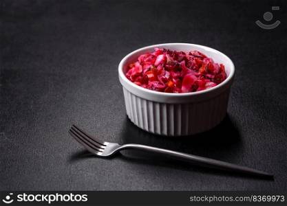 Vinaigrette,  raditional ukrainian beetroot salad with boiled vegetables, pickled cucumbers, sour cabbage, olive oil and green canned peas. Vegetarian healthy dinner. Traditional ukrainian beetroot salad vinaigrette on a white plate on a black concrete or slate background