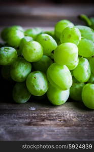 Vine of green grapes on rustic wooden background