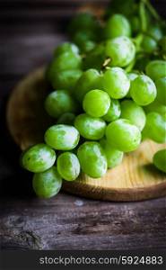 Vine of green grapes on rustic wooden background
