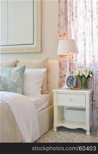 vintage bedroom interior with decorative table lamp, alarm clock and flower on white table