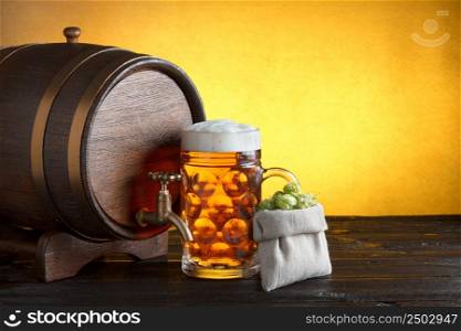 Vintage beer barrel with huge glass of beer and burlap bag with fresh hops on wooden table still life