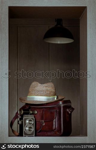 Vintage binocular on Vintage two lens photo camera front of Straw fedora hat on Vintage brown leather bag in Square wooden frame Interior. Vintage style traveling concept, Selective focus.