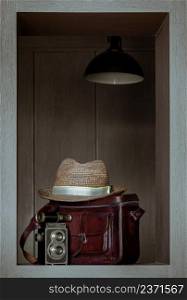 Vintage binocular on Vintage two lens photo camera front of Straw fedora hat on Vintage brown leather bag in Square wooden frame Interior. Vintage style traveling concept, Selective focus.