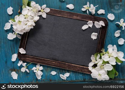 Vintage blank chalkboard or school slate is on an old blue rustic wooden background with white apple flowers, with space for text or message