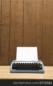 Vintage blue typewriter on desk with wood paneling.