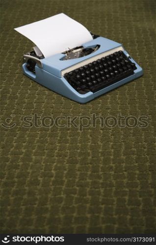 Vintage blue typewriter on green carpet.