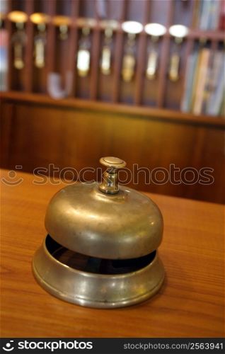 Vintage brass bell on hotel front desk with blurred key rack in the background. Very shallow depth of field with focus on the button.