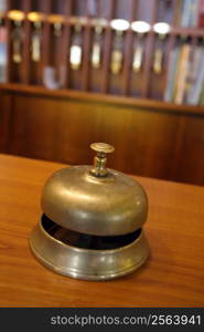 Vintage brass bell on hotel front desk with blurred key rack in the background. Very shallow depth of field with focus on the button.