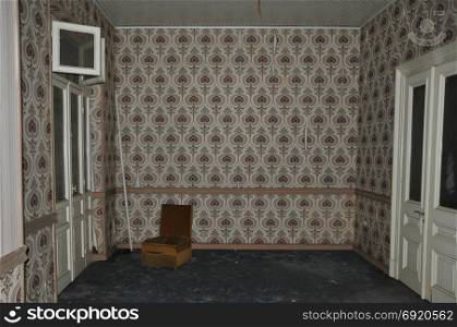 Vintage chair and wall with retro wallpaper pattern in empty living room of an abandoned house.