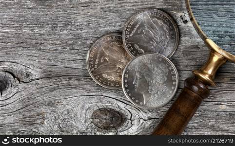 Vintage collection of US Morgan silver dollars with magnifying glass on rustic wooden boards in flat lay view