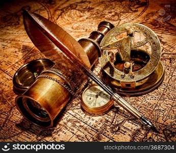 Vintage compass, goose quill pen, spyglass and a pocket watch lying on an old map.