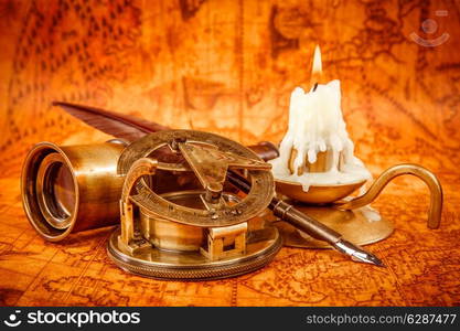 Vintage compass, magnifying glass, quill pen, spyglass lie on an old ancient map in 1565 with a lit candle. Vintage still life.