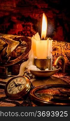 Vintage compass, pocket watch lie on an old ancient map with a lit candle