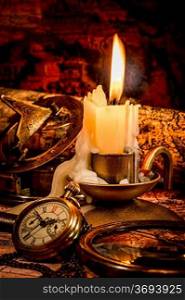 Vintage compass, pocket watch lie on an old ancient map with a lit candle