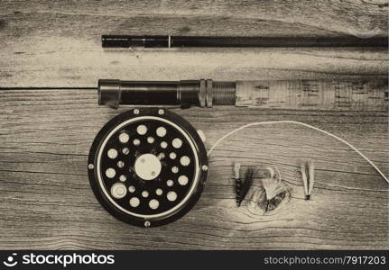 Vintage concept of an antique fly fishing reel and rod on rustic wood. Layout in horizontal format.