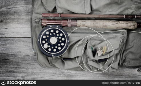 Vintage concept of an antique fly fishing reel and rod with vest and flies on rustic wood. Layout in horizontal format.