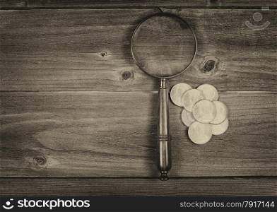 Vintage concept of an antique round shaped magnifying glass and a pile of old silver dollar coins on rustic wood