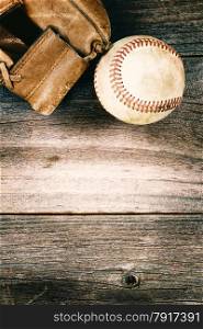 Vintage concept of an old baseball and weathered leather mitt on rustic wood. Format in vertical layout.