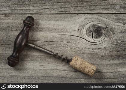 Vintage concept of an old corkscrew with attached cork on rustic wooden boards.