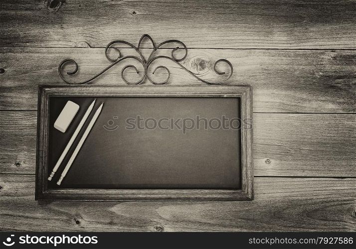 Vintage concept of an old fashion chalkboard, pencils and eraser on rustic wood. Layout in horizontal format.