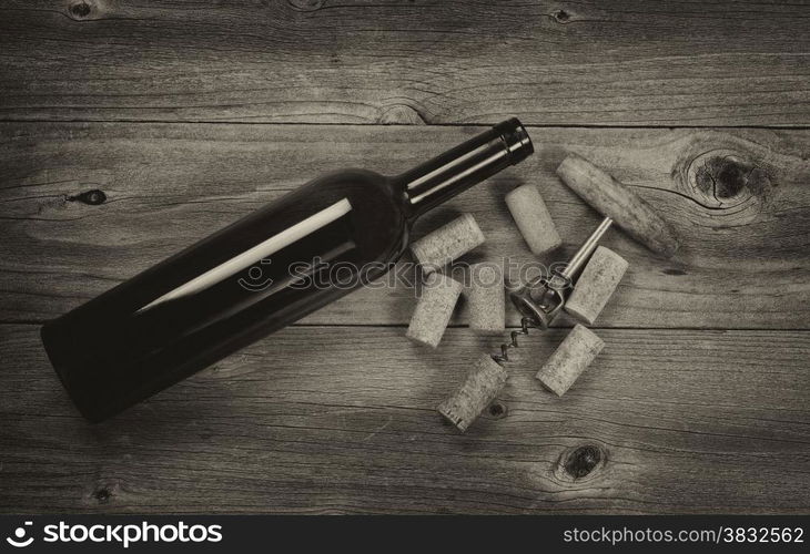 Vintage concept of antique corkscrew, used corks, and wine bottle on rustic wooden boards. Top view angled shot in horizontal format with vignette border.