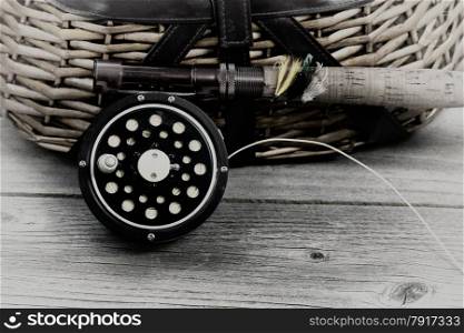 Vintage concept, with grain, of an antique fly fishing reel, rod, and artificial flies in front of creel with rustic wood underneath. Layout in horizontal format.