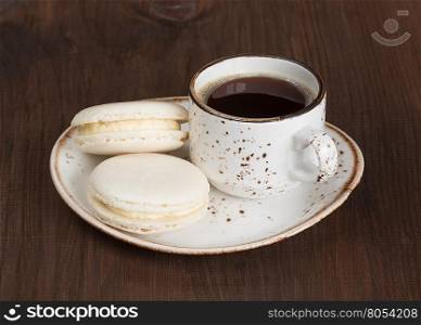 Vintage cup of black coffee and two macaroon cakes on a dark wooden table