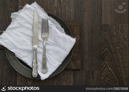 Vintage cutlery on muslin cloth on pewter plate with rustic wooden backgorund